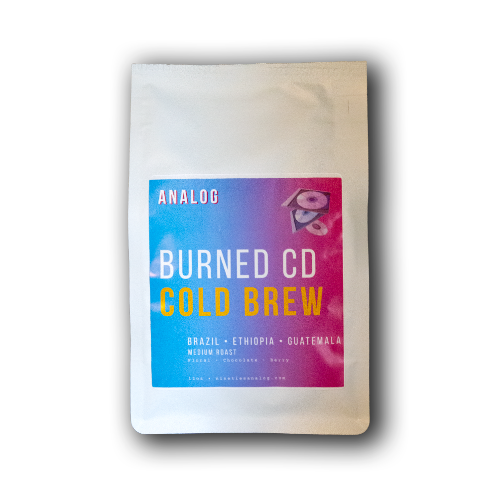 A white stand-up pouch of Analog Burned CD Cold Brew coffee with a colorful blue-to-pink label, shown on a black background with a drop shadow.