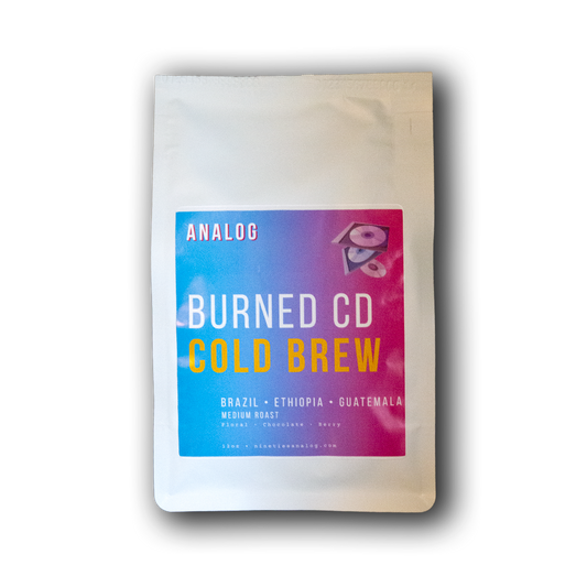 A white stand-up pouch of Analog Burned CD Cold Brew coffee with a colorful blue-to-pink label, shown on a black background with a drop shadow.
